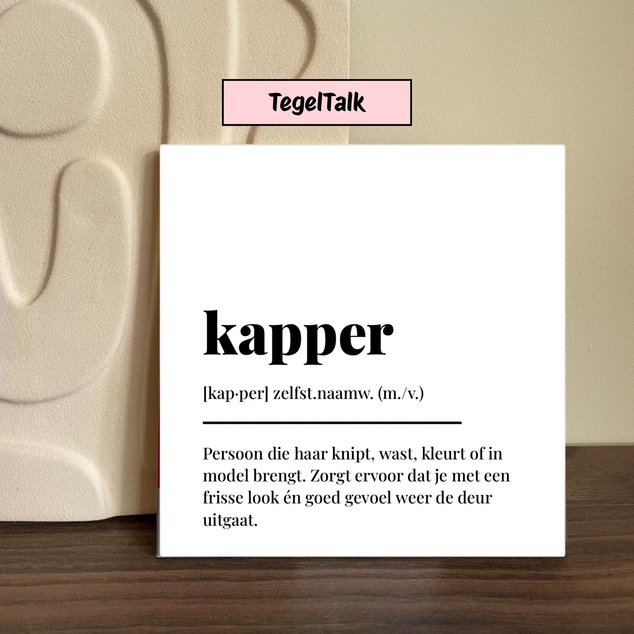 Wit tegeltje met de tekst ‘kapper’ in woordenboekstijl op houten ondergrond – categorie TegelTalk