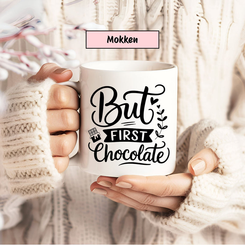 Witte mok met zwarte quote ‘But First Chocolate’ vastgehouden door iemand in een cosy gebreide trui – categorie Mokken.
