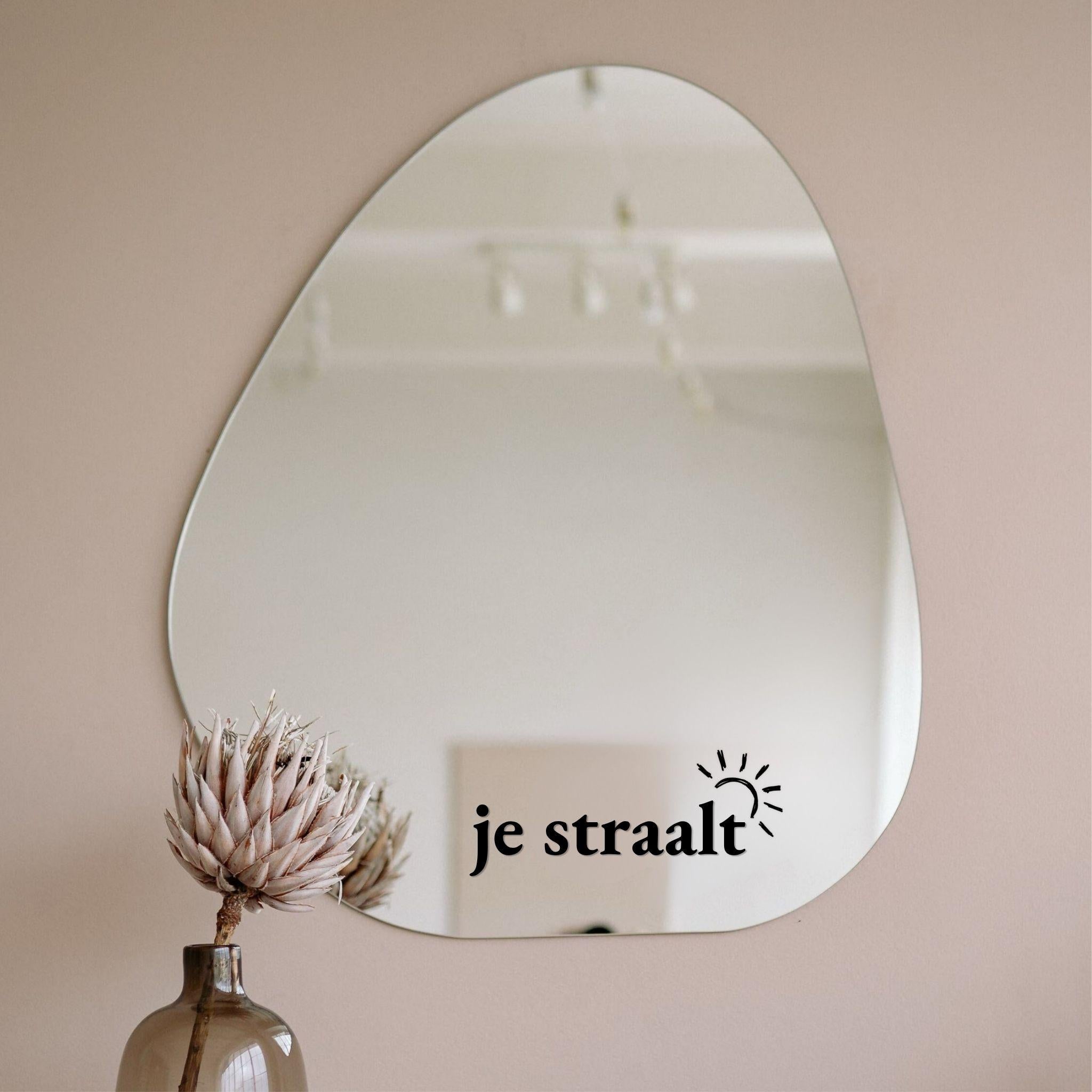 Zwarte spiegelsticker met tekst je straalt en zonnetje op een organische spiegel in een licht interieur met vaas en droogbloem