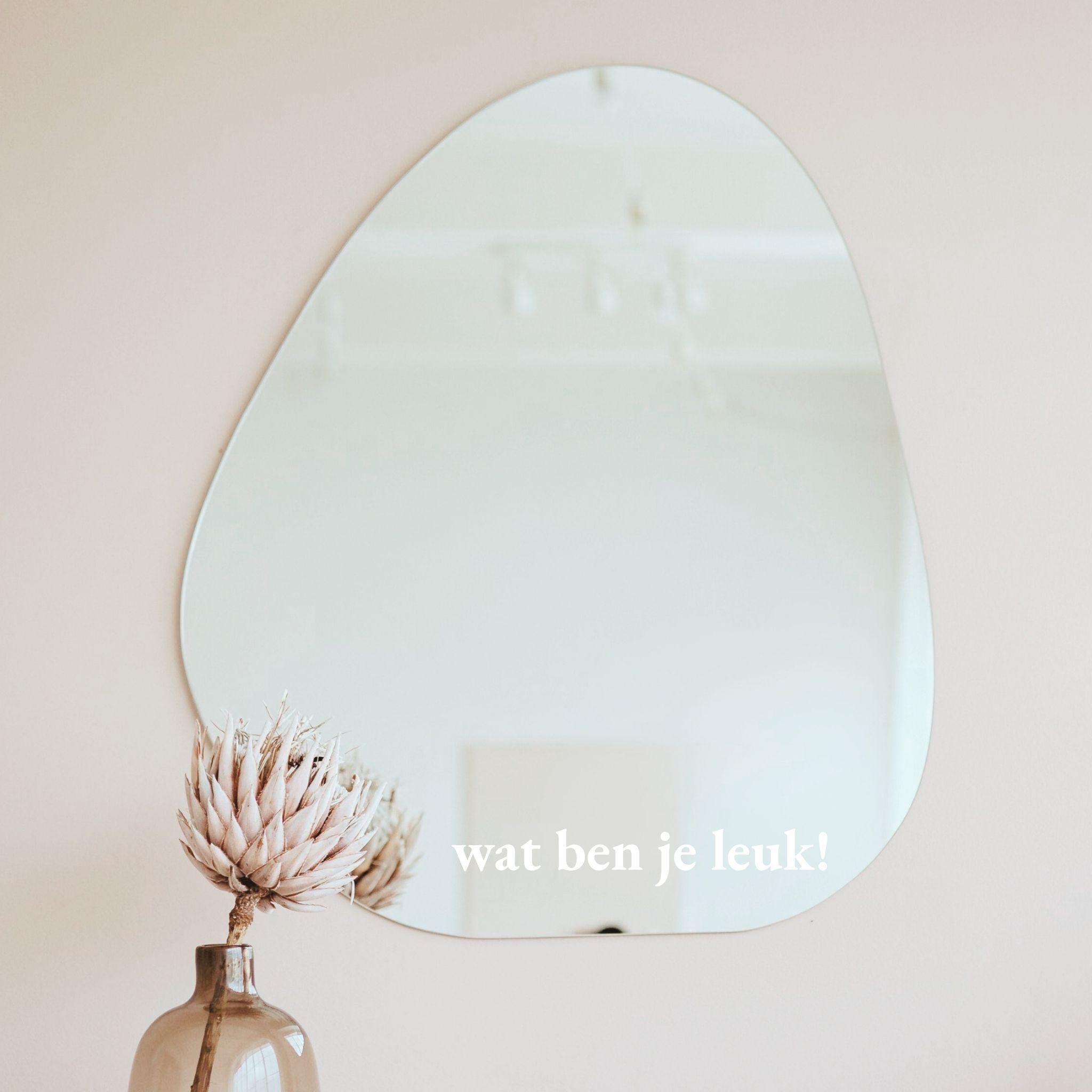 Witte spiegelsticker met tekst wat ben je leuk op een organische spiegel in een licht interieur met vaas en droogbloem