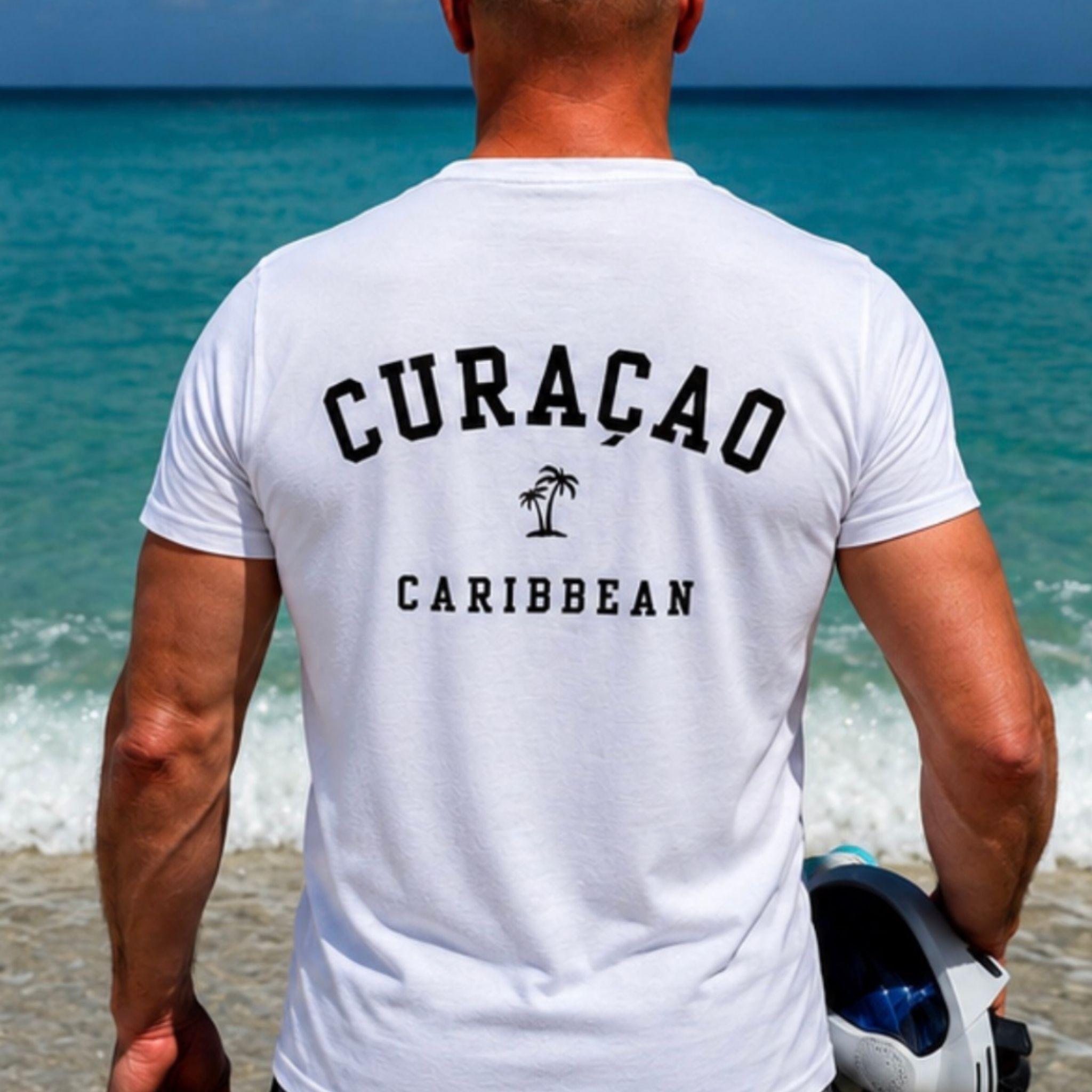 Man draagt een wit Curaçao Caribbean T-shirt op het strand met een rugopdruk in college-stijl en een palmboom.