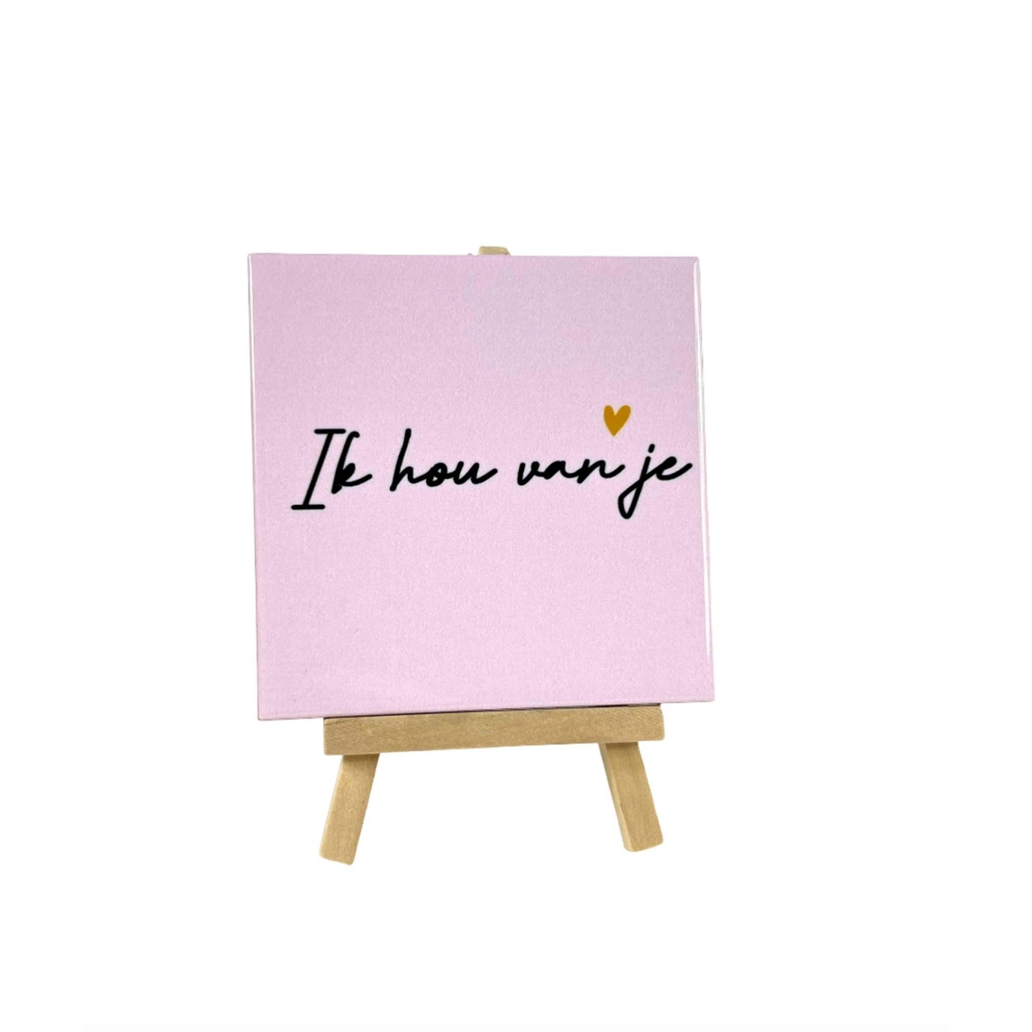 Keramisch tegeltje met de tekst Ik hou van je en een klein hartje op een roze achtergrond geplaatst op een houten standaard Studio DSigns