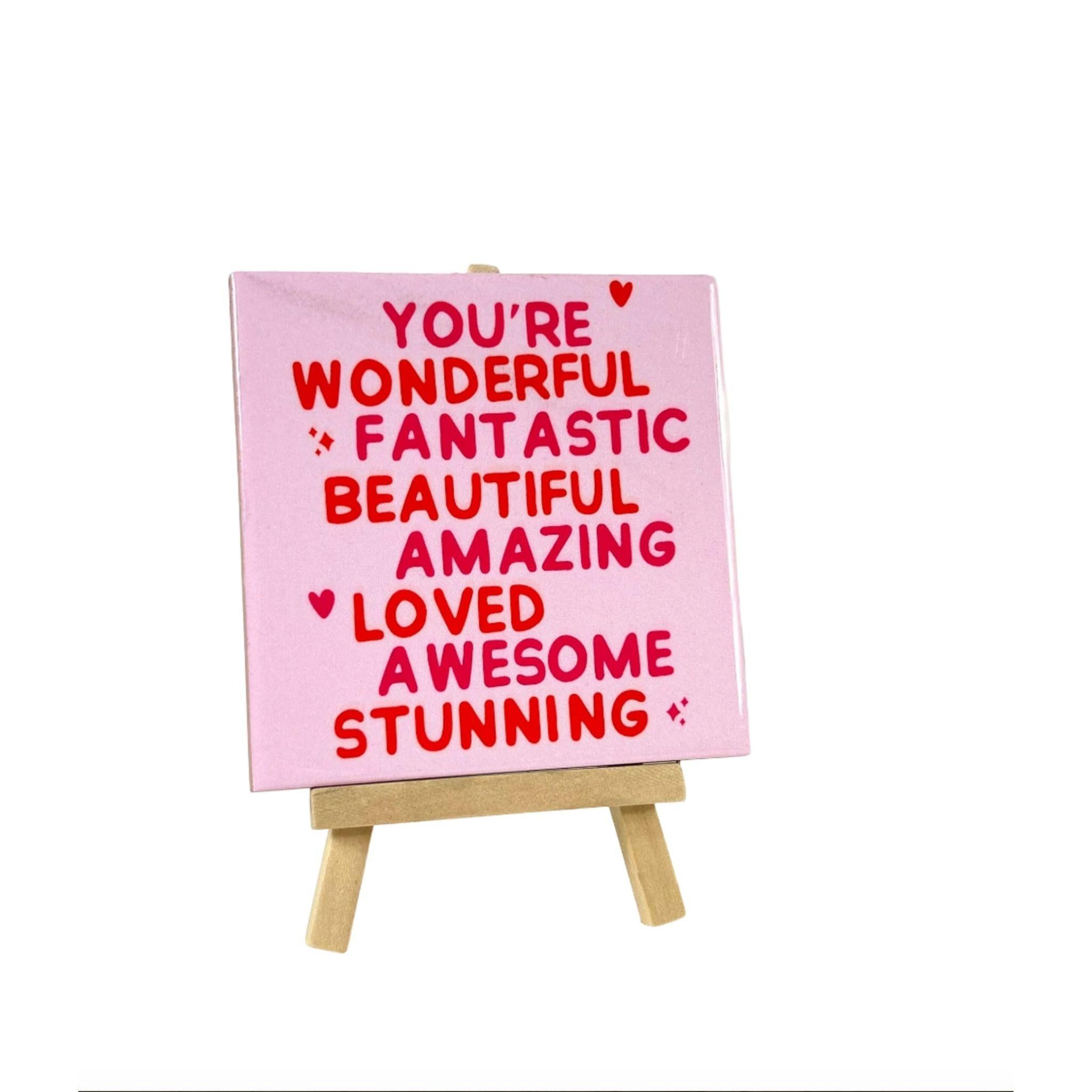 Keramisch tegeltje met positieve woorden zoals wonderful fantastic beautiful en amazing op een roze achtergrond geplaatst op een houten standaard Studio DSigns